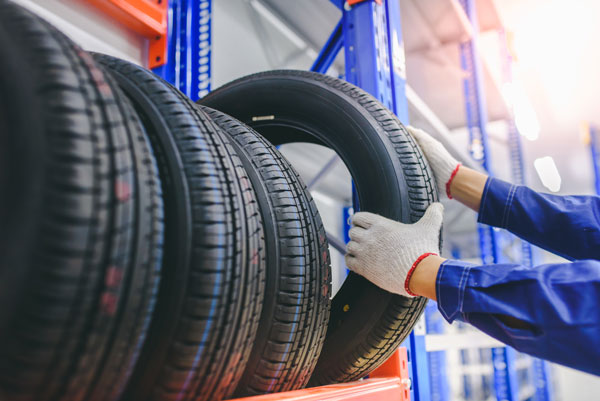 Asian male tire changer In the process of checking the condition of new tires in stock so that they can be replaced at a service center or auto repair shop.