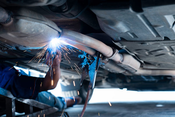 The hand of a mechanic or welder is fixing a car exhaust system by welding the exhaust pipe.