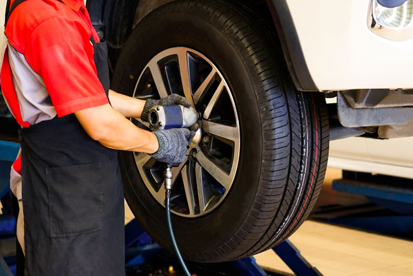 a worker is using a drill to tighten a nut while changing a car tire.