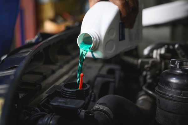 Auto mechanic filling Pre-mixed Super Long Life Coolant fluid in car radiator fill hole.