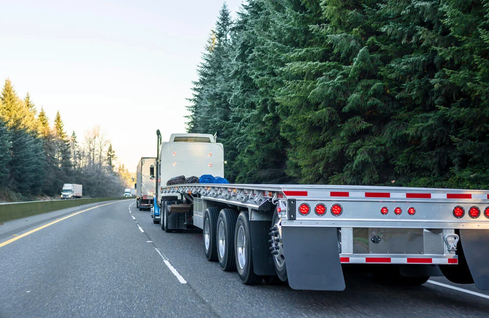 Big rig long haul powerful semi truck with empty light weight aluminum flat bed semi trailer running on the winter road