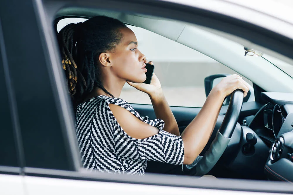 Side view of African serious woman using mobile phone and has a conversation while driving her car
