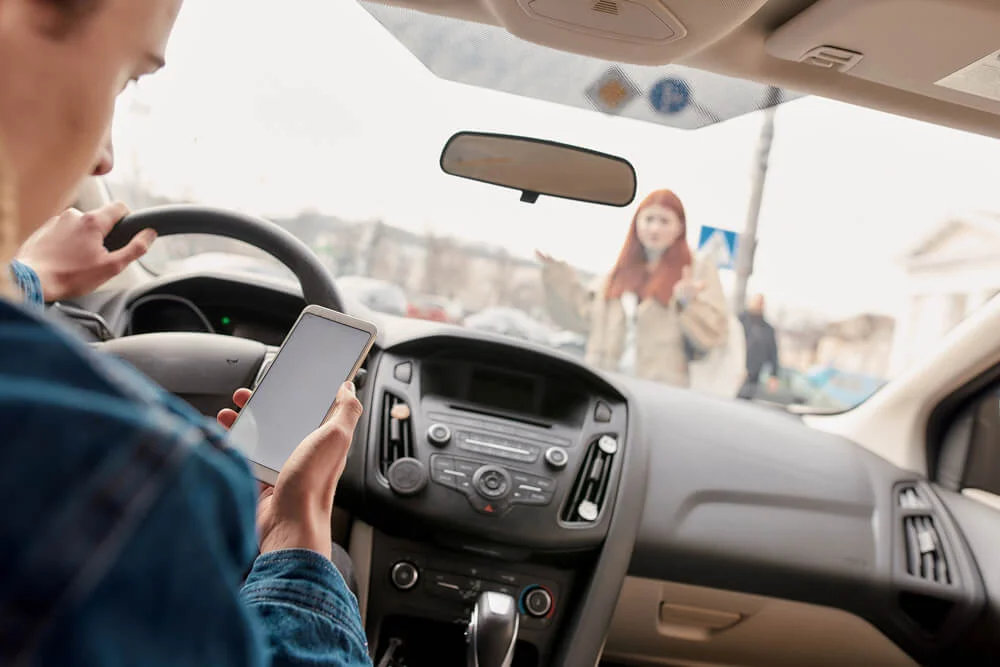 Distracted young male driver looking at the screen of his mobile phone while running over a pedestrian