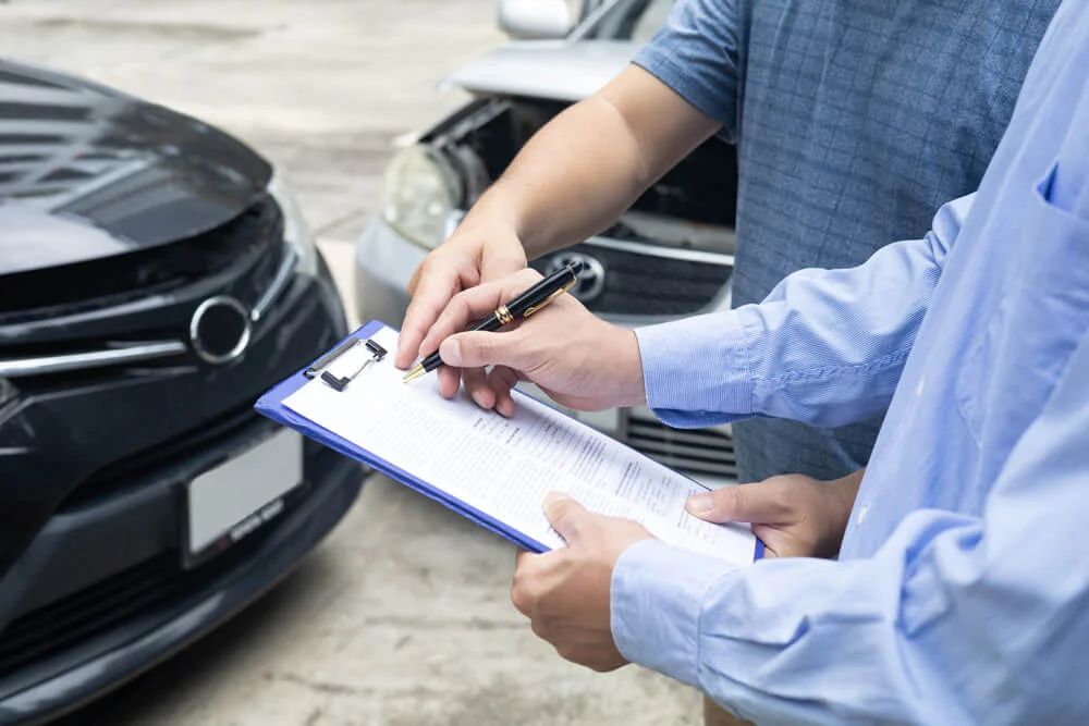 insurance officer writing on clipboard while insurance agent examining black car after accident