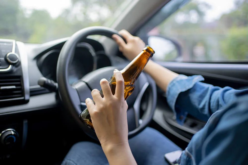 Hand holding alcoholic bottle while driving, Close-up.