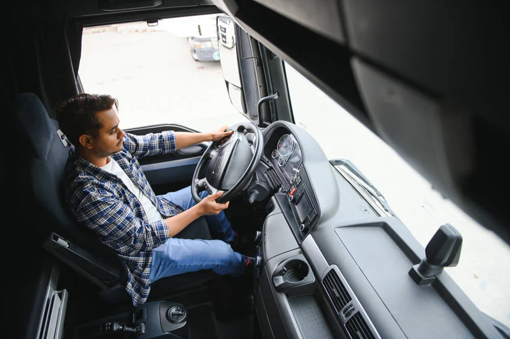 A young Indian male truck driver sits behind the wheel.
