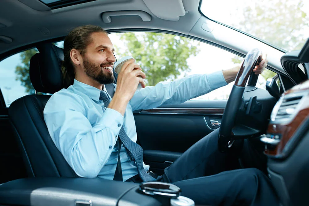 Portrait Of Business Man Driving Car. Succesful Young Smiling Businessman Drinking Coffee From Paper Cup While Driving Car