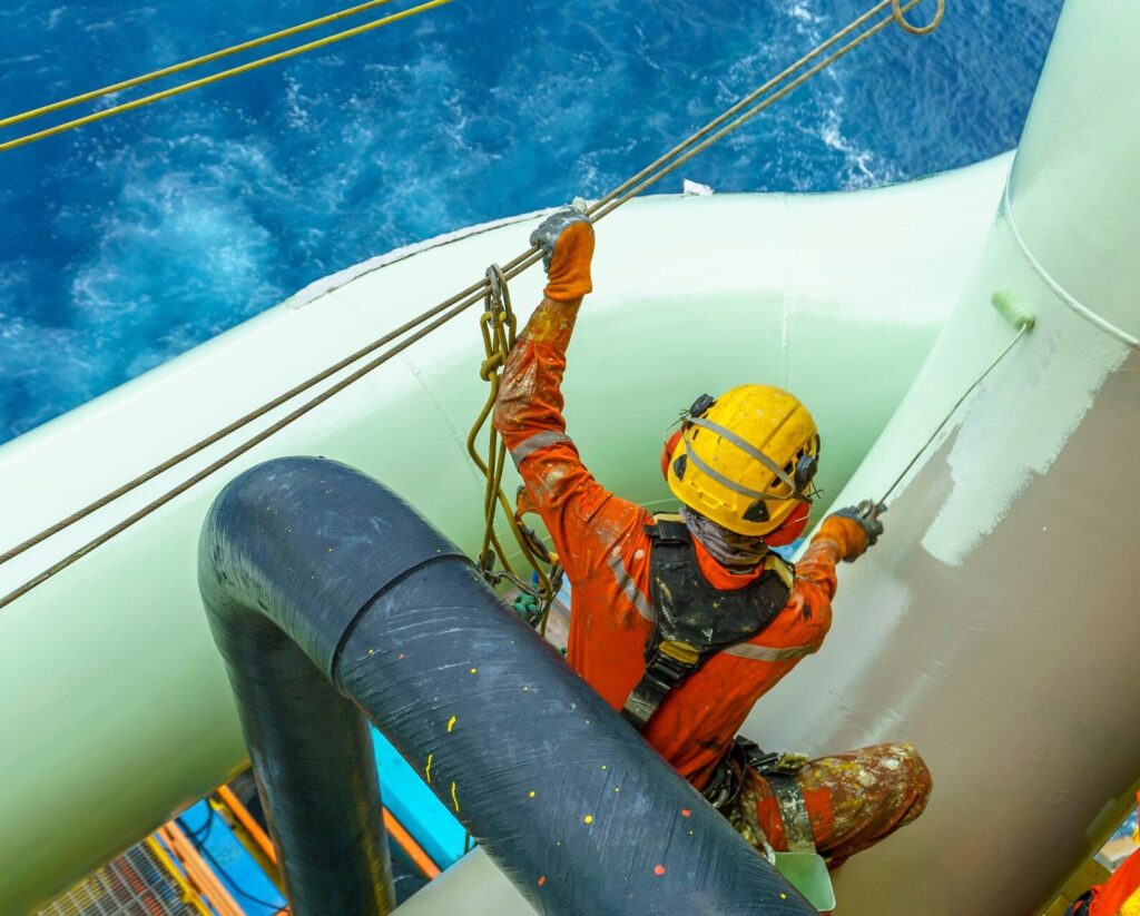 Working at height. An abseiler wearing complete Personal Protective Equipment (PPE) sitting on gas pipeline for painting activities.
