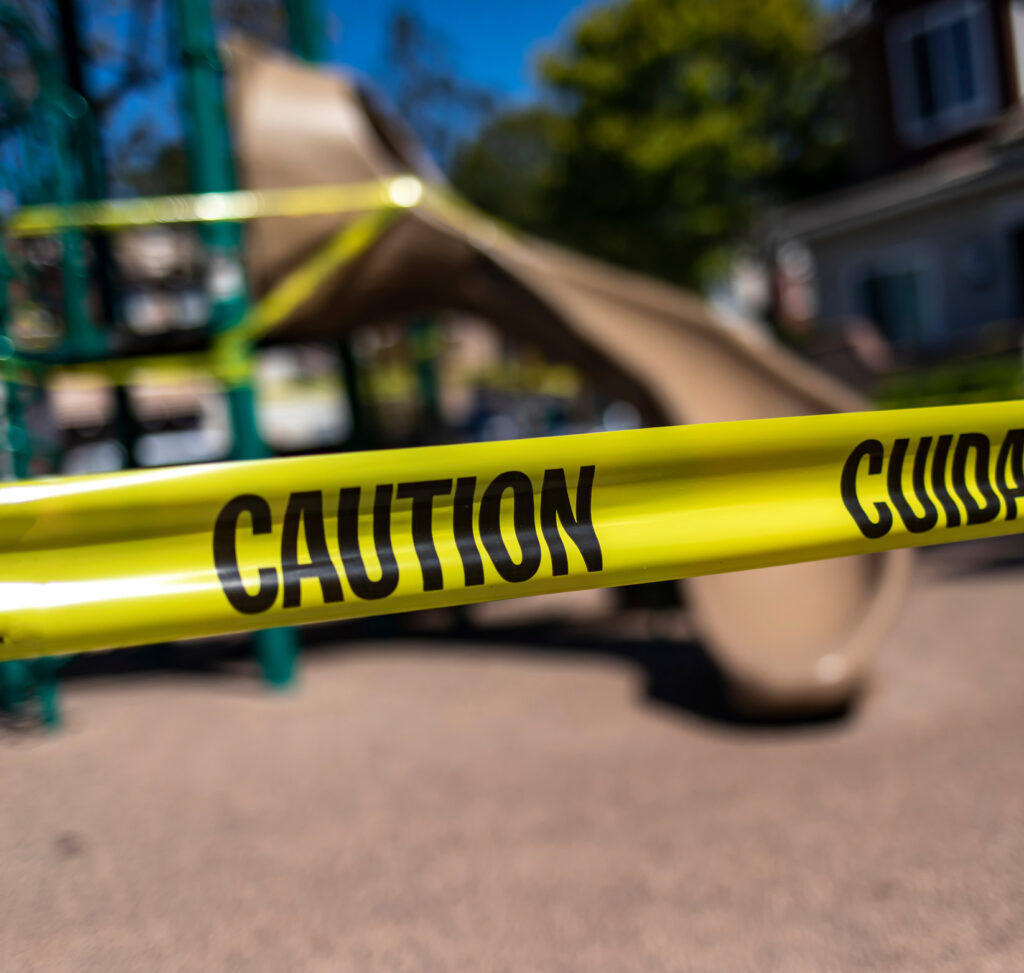 Yellow caution tape in english and spanish barring access to playground equipment at a park.