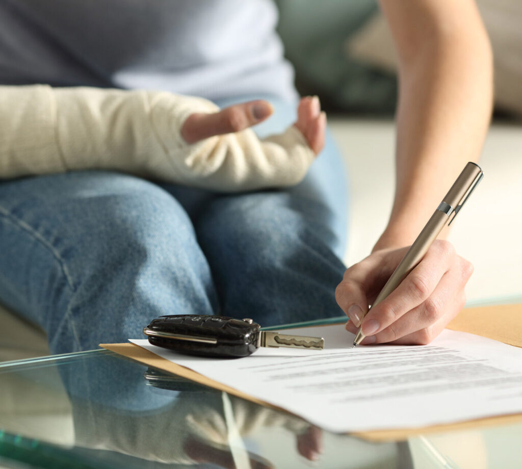 Close up of a lady hands with broken arm signing insurance document after car accident at home