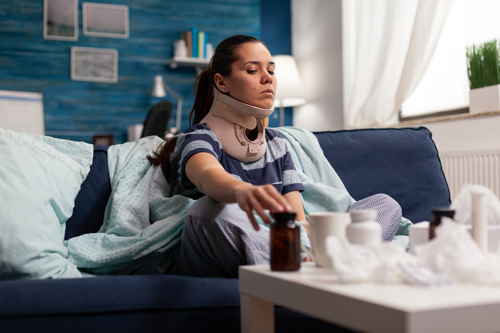 Woman in neck brace suffering from pain on sofa after bad accident injury.