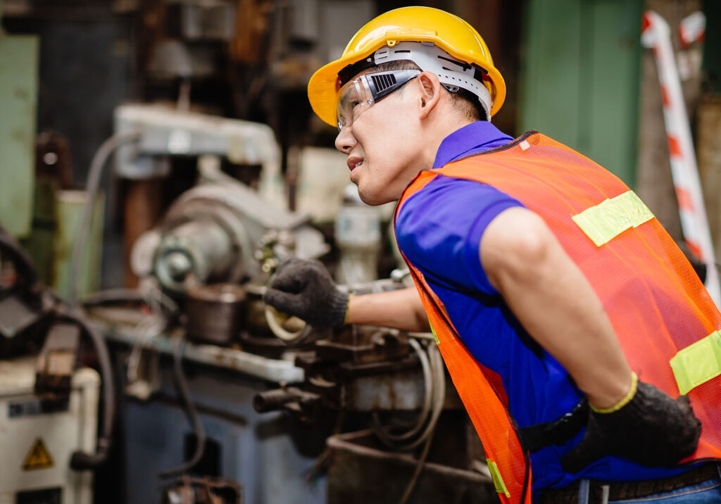 Asian worker working hard in industrial factories suffer from back waist pain while working on machines.
