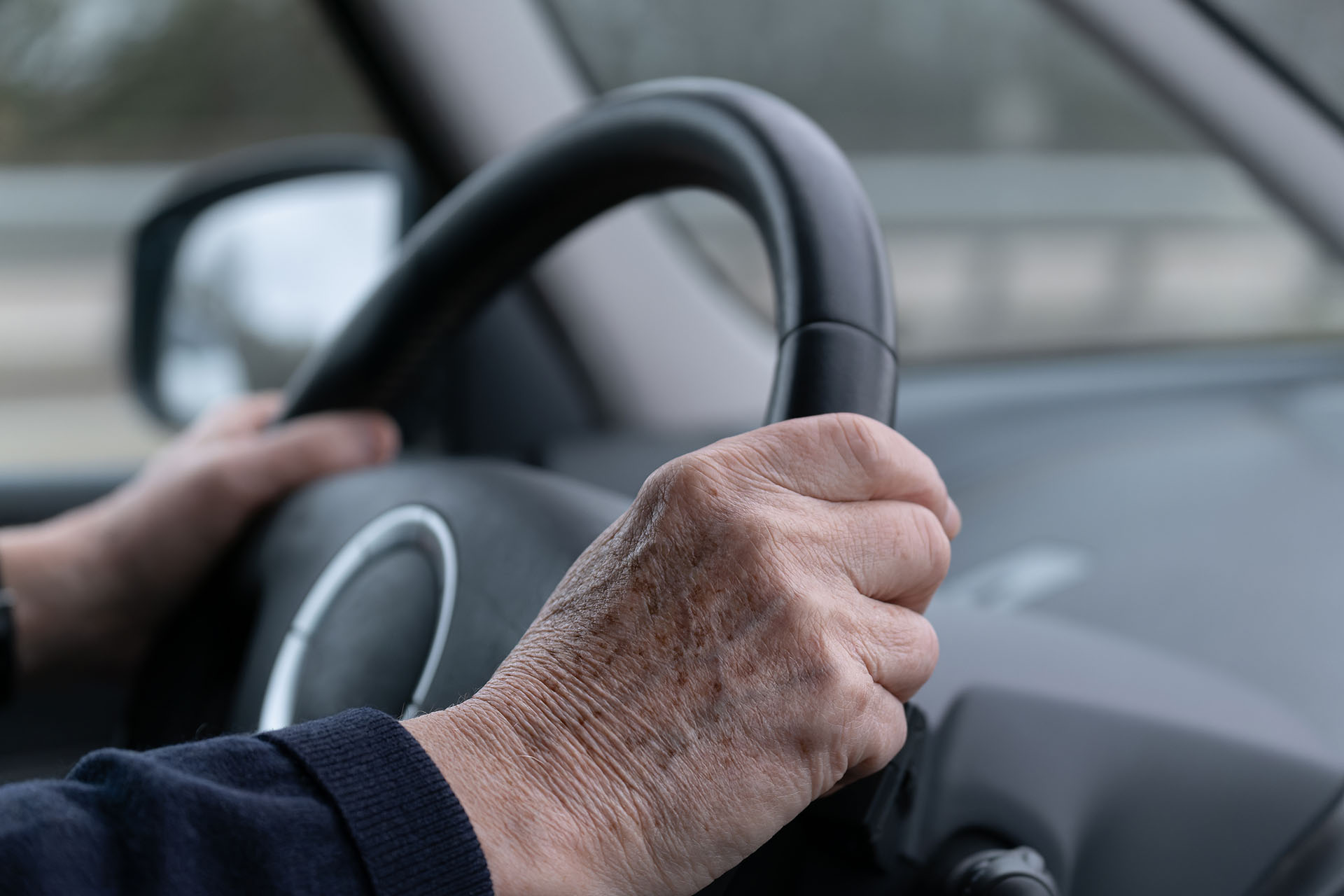An elderly person driving a car with their hands on the wheel