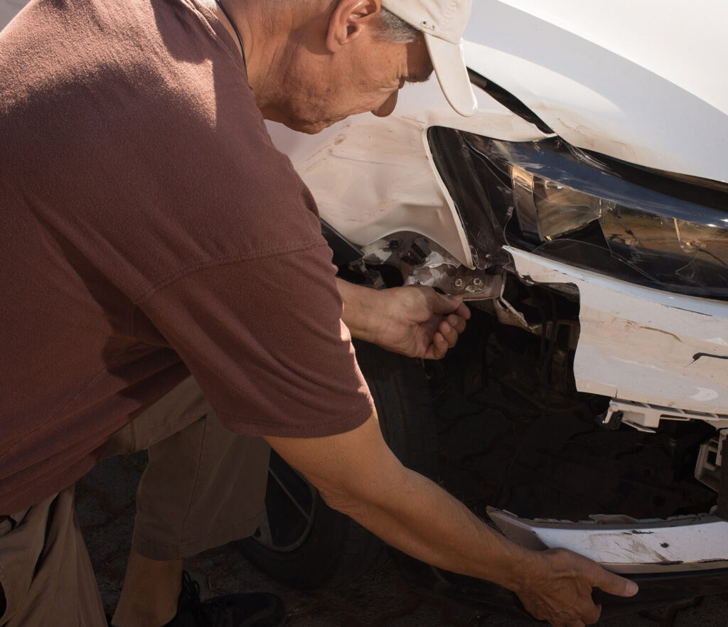 Man checking out the damage to the right front end of his car that was in a collision