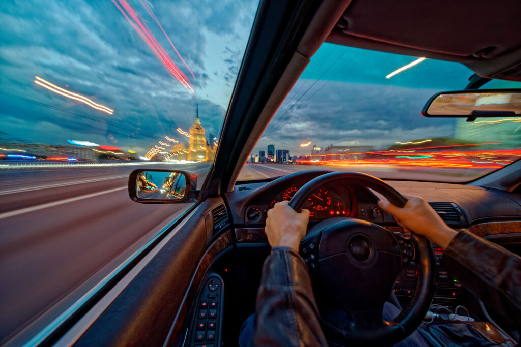 Movement of the car at night at high speed view from the interior with driver hands on wheel