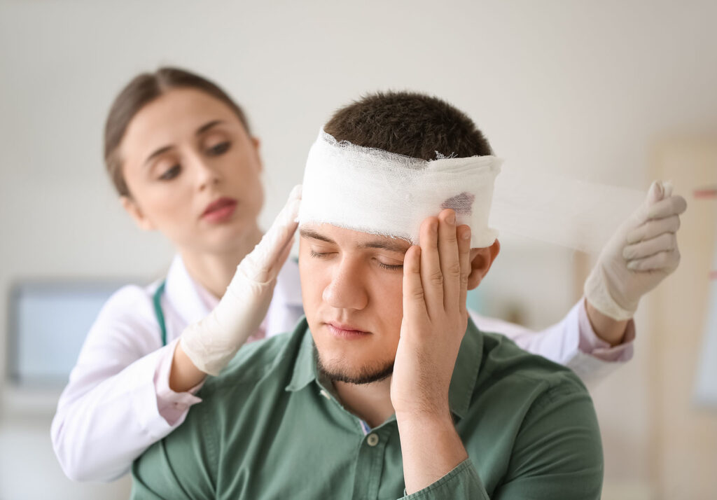 Doctor applying bandage onto head of young man in clinic