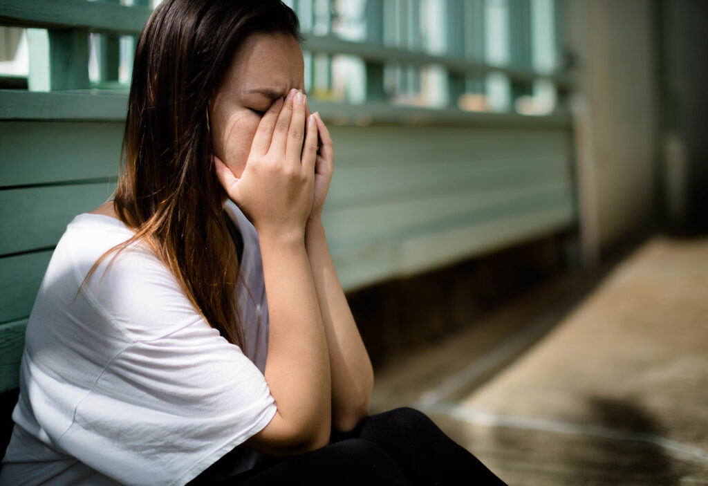 Depressed woman sitting with her hands covering her face overwhelmed with emotion
