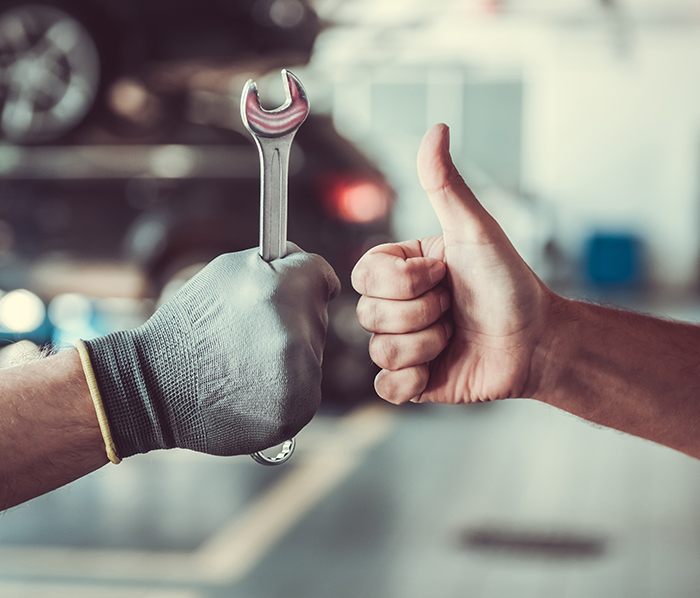 Two hand of technician, On the right hand the mechanic has gloves while holding a wrench, On the left hand the mechanic is doing a thumbs up